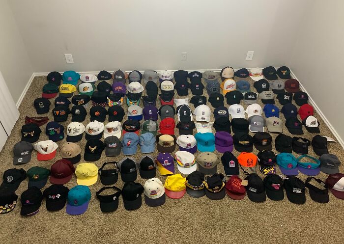 A large collection of various colorful baseball caps neatly arranged on a carpeted floor showing hat obsession.
