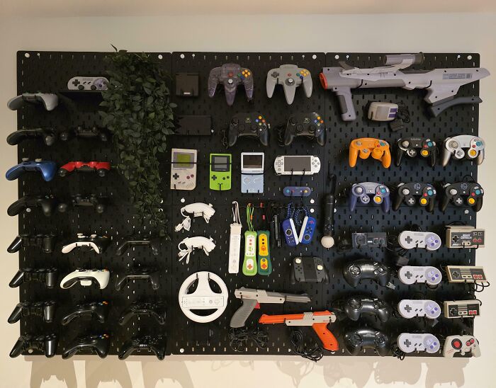 Wall-mounted collection of vintage and modern gaming controllers and handheld consoles showing video game obsession.