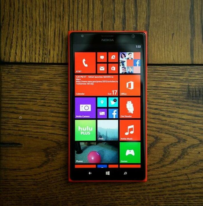 Nokia smartphone displaying classic 2010s Windows interface with colorful app tiles on a wooden table.