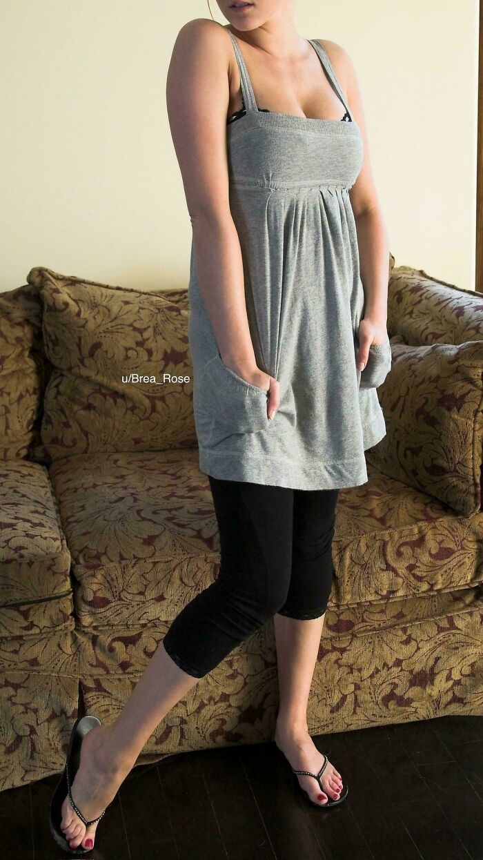 Young woman in casual 2010s style dress and leggings standing near vintage patterned sofa indoors.