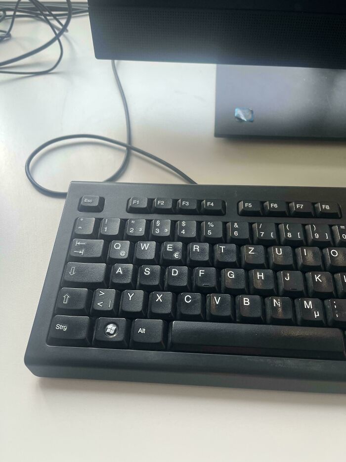 Black wired keyboard on a white desk with a computer monitor, evoking nostalgia for tech in the 2010s era.