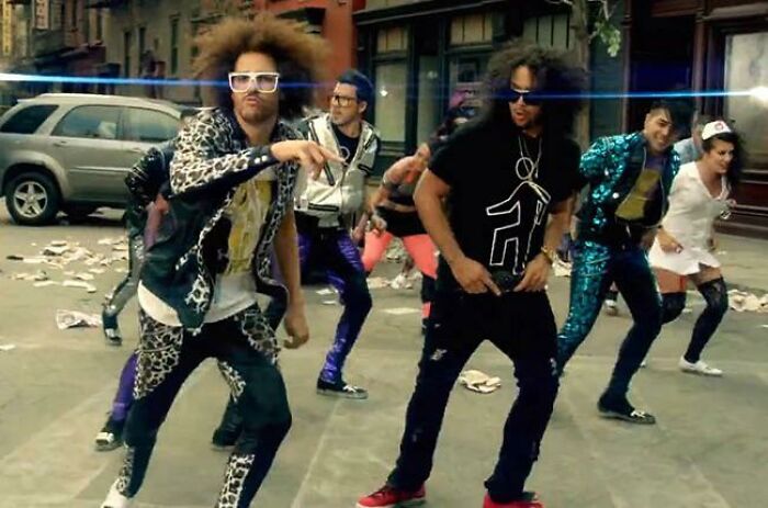 Dancers in colorful 2010s style outfits performing on a city street, capturing iconic 2010s nostalgia and vibes.