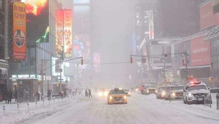 Snow-covered city street with cars and pedestrians navigating during a 2010s winter scene in urban traffic.