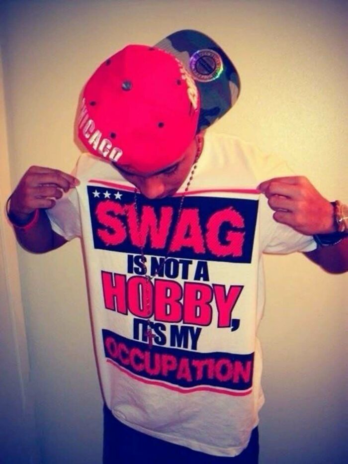 Young man in a red Chicago cap showing a 2010s style shirt reading swag is not a hobby, it's my occupation, 2010s fashion nostalgia