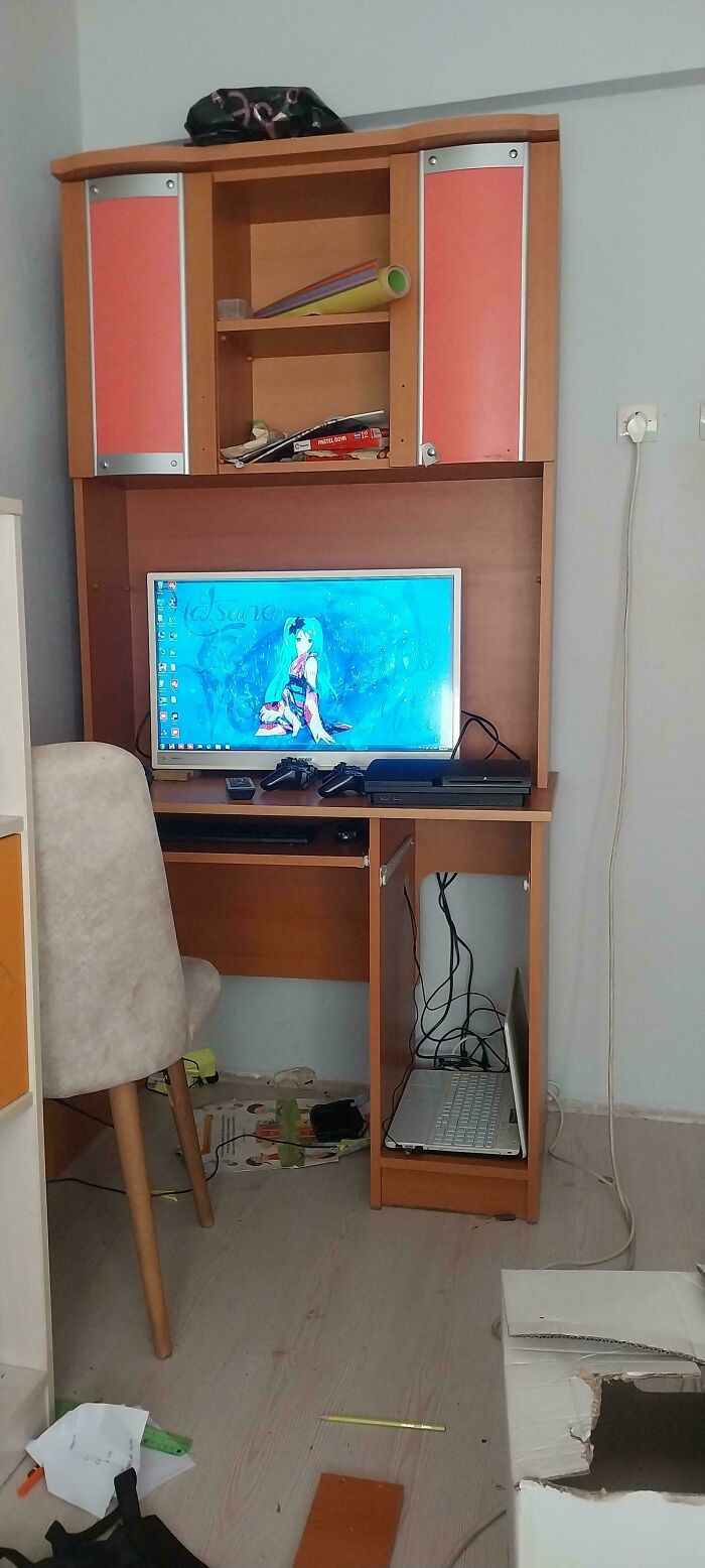 Wooden computer desk with gaming console, controllers, and anime wallpaper, evoking nostalgia of better 2010s setup.