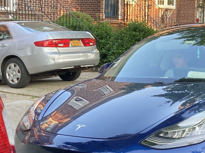 Person sitting inside a Tesla car parked on a residential street, highlighting entitled Karens with no sense of shame.