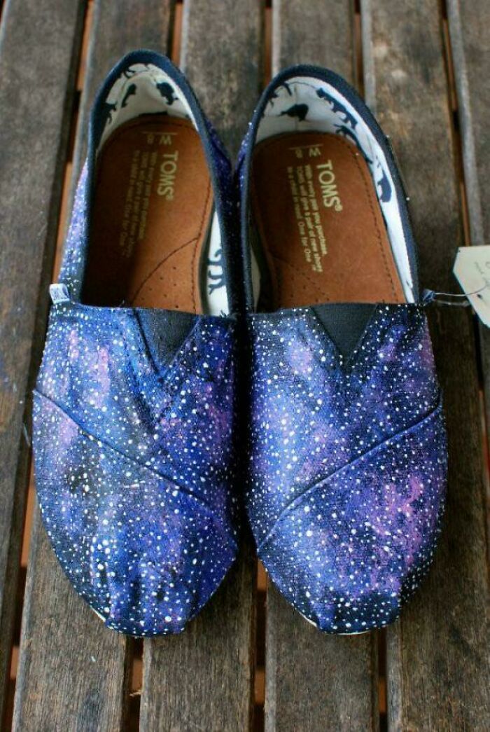 Galaxy patterned TOMS shoes in blue and purple tones placed on a wooden surface, reflecting 2010s nostalgic fashion trends.