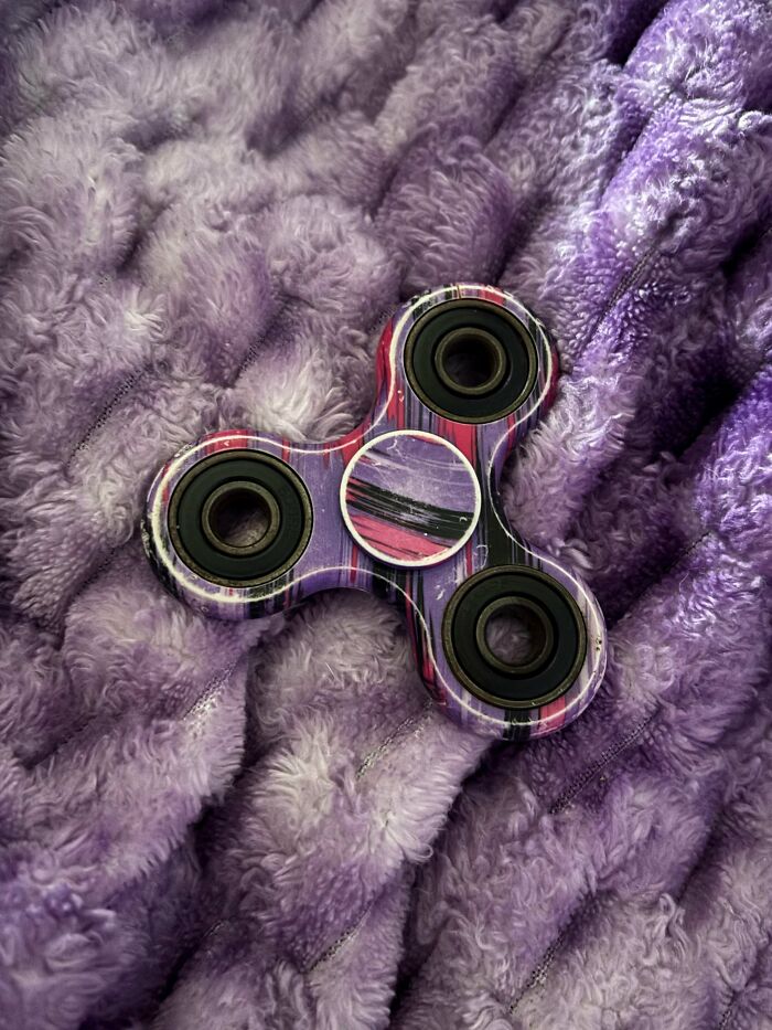 Fidget spinner with colorful design resting on a soft purple textured fabric, reminiscent of 2010s nostalgia.