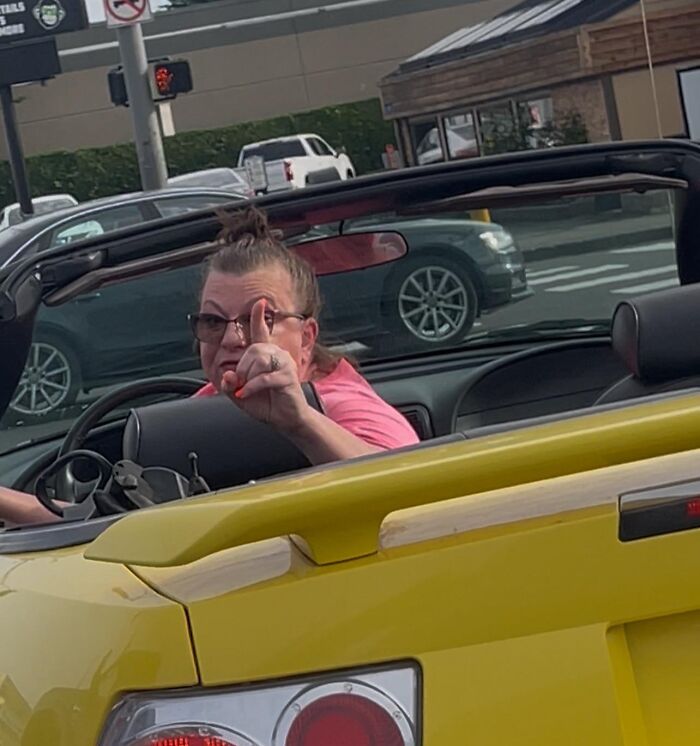 Woman driving yellow convertible car, pointing finger aggressively, showcasing entitled Karen behavior on busy street.