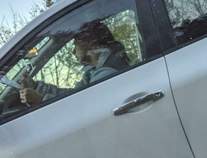 Man driving a car, holding a phone, illustrating a story about entitled Karens missing a sense of shame.