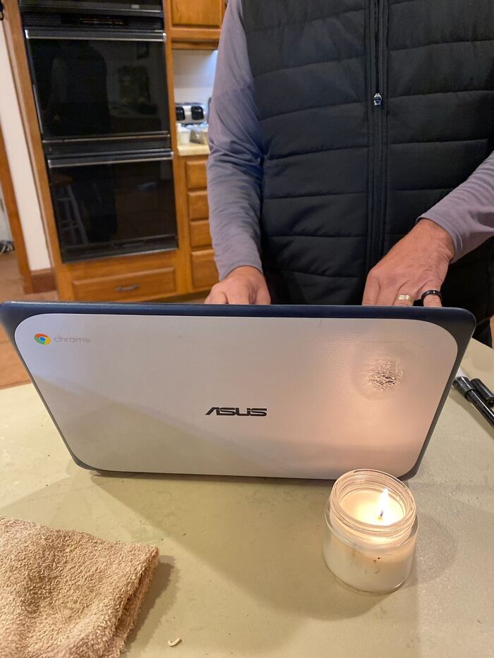 Person standing behind laptop with burned spot on lid next to lit candle, showing a disaster that could go wrong.