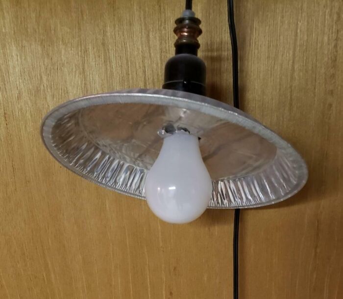 Improvised light fixture made with a foil pie pan reflecting light from a bulb, showcasing a technically works hack.