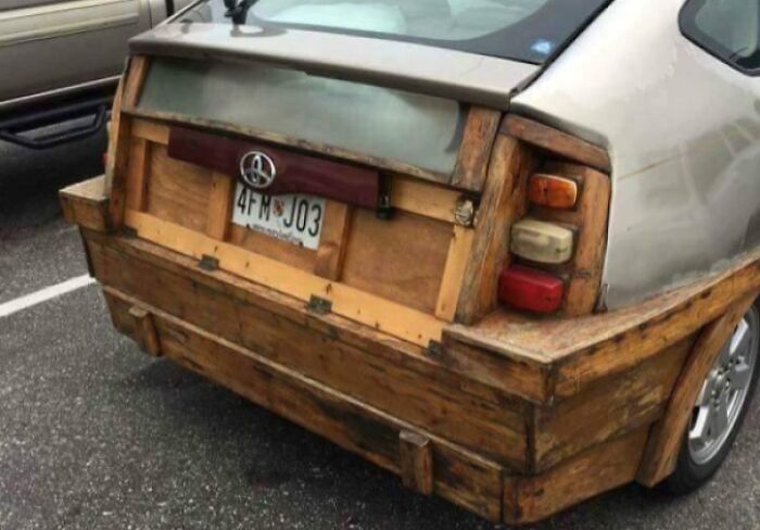 Car with a wooden rear bumper and trunk replacement, showcasing a technically works but makeshift solution to vehicle damage.