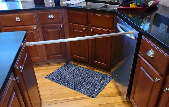 Kitchen cabinets with a dishwasher door held open by a tension rod as a funny, technically works solution to a problem.