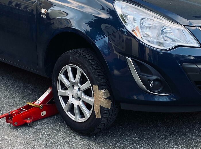 Car tire patched with tape while lifted on a red jack illustrating technically works funny problem solutions.