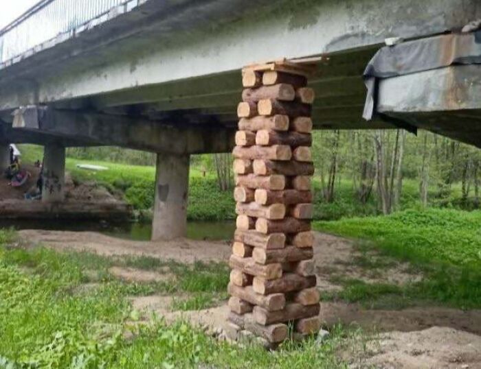 Bridge supported by a stack of uneven wooden logs as a hilariously dumb yet technically works solution to structural support.