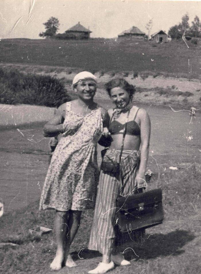 Candid old photos: Two women in swimwear by a river, with houses on a hill in the background.