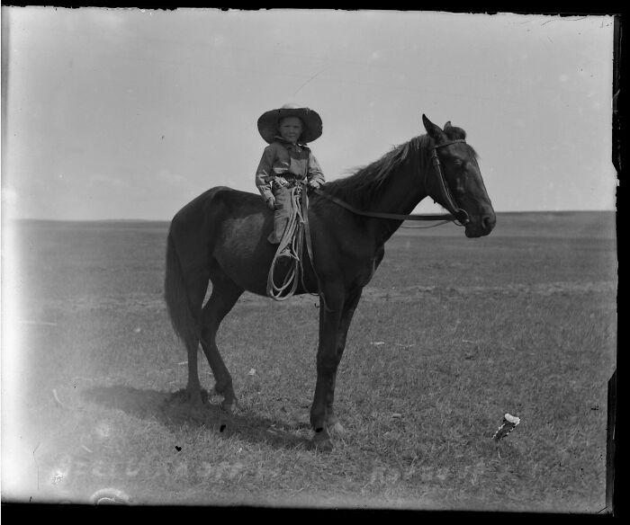 A candid old photo of a child in a cowboy hat on horseback, revealing what the world looked like generations ago.