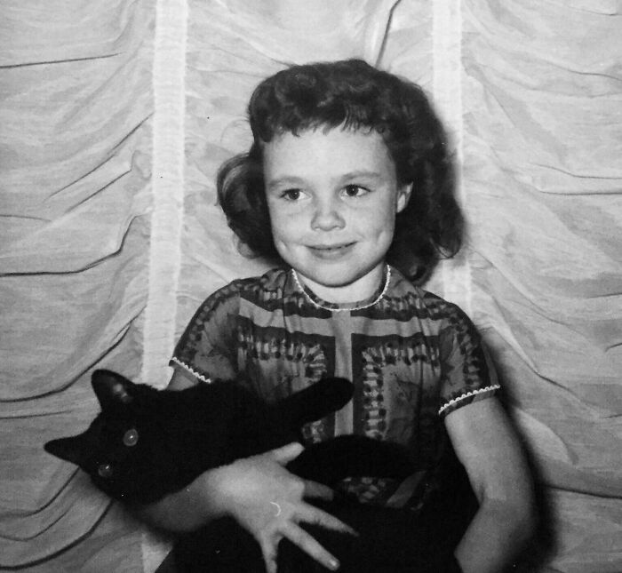 A candid old photo of a young girl with dimples holding a black cat, revealing what the world looked like generations ago.