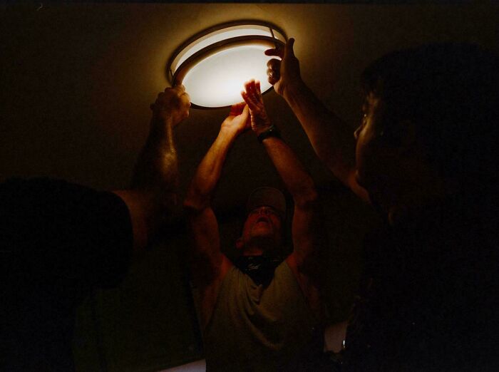 Three pairs of hands installing a ceiling light fixture in Accidental Renaissance lighting