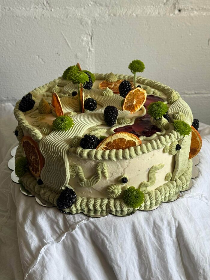 Decorative dessert cake with green frosting, blackberries, and dried orange slices
