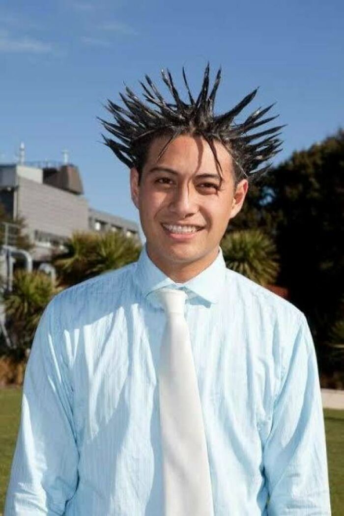 A smiling man wearing a light blue shirt and white tie, with an unfortunate haircut styled into spikes.