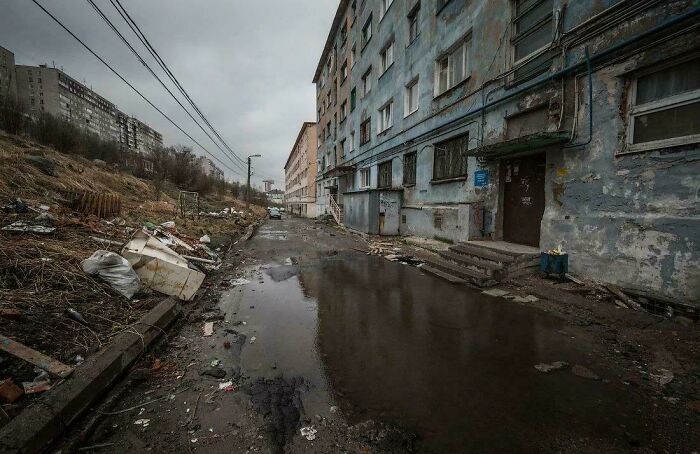 Dilapidated urban hell apartment block with wet street and scattered trash