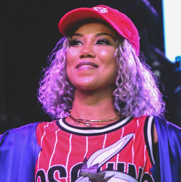 Jhen&eacute; Aiko smiling on stage wearing a red cap and basketball jersey, highlighting her music career presence.