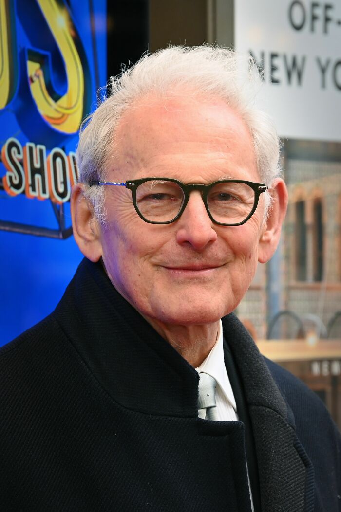 Victor Garber wearing glasses and a black coat, smiling at an outdoor event showcasing career highlights.