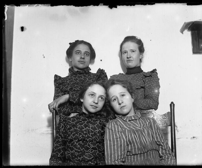 Four women pose together, their serious expressions captured in a candid old photo from generations ago.