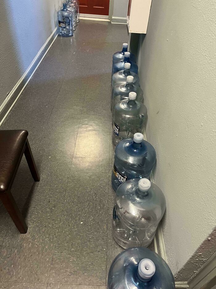 Empty water jugs lined up multiple times in a narrow hallway, illustrating unusual neighbors from remote places.