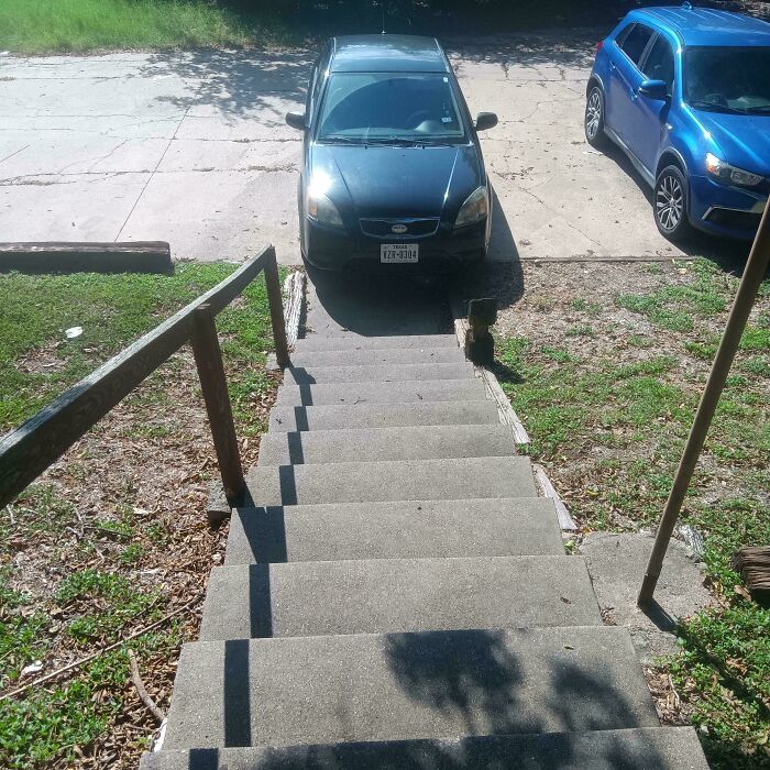 Concrete stairs leading down to a narrow driveway with two parked cars, illustrating unusual neighbors in rural areas.