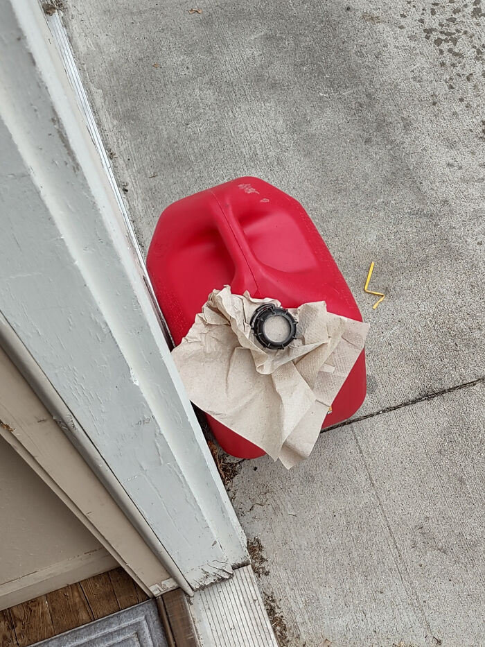 Red gas container with a torn paper towel and cap on concrete near a house entrance, illustrating odd neighbor behavior.
