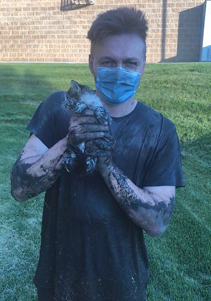 Man covered in mud wearing a mask holding a dirty kitten representing animals saved from awful conditions and given a second chance.