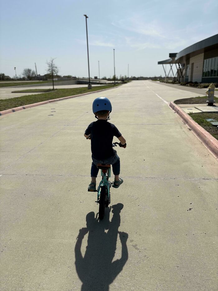 A young child in a helmet rides a bicycle down an empty road, a wholesome image of a great dad's guidance.
