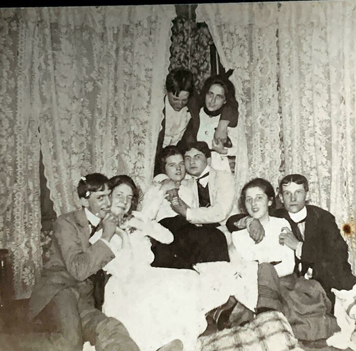 Group of people in vintage clothing posing closely together in a bizarre throwback moment from the past.