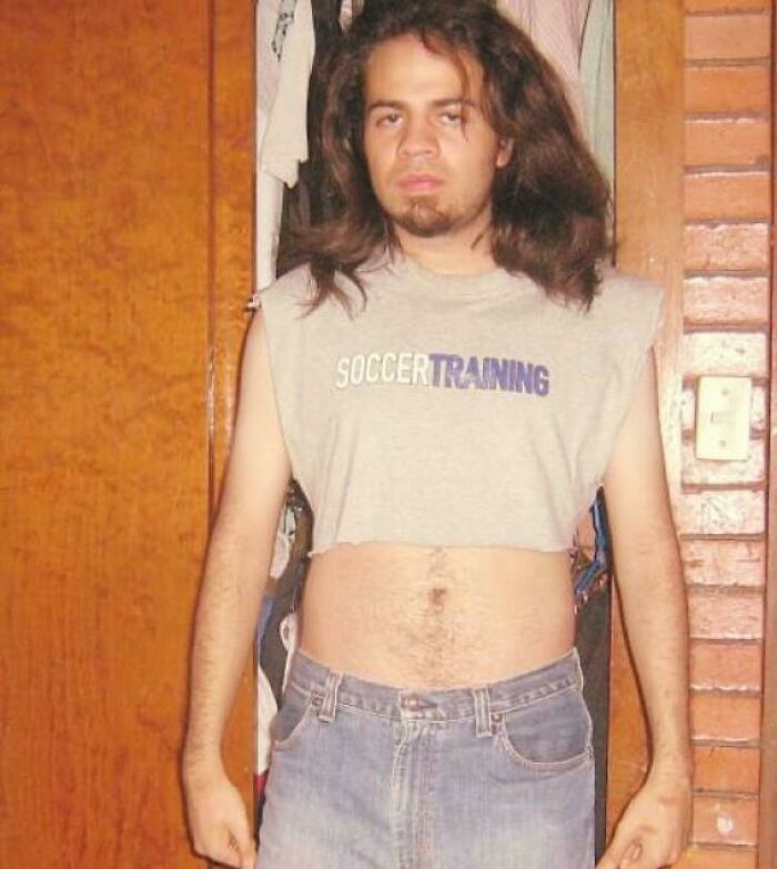 Young man with long hair wearing a cut-off soccer training shirt and high-waisted jeans in a bizarre throwback moment.