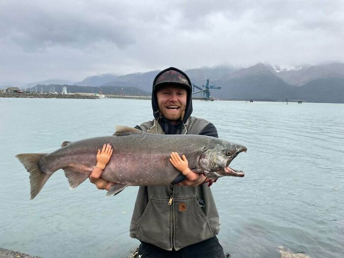 Man holding a large fish with tiny realistic hands attached, an unedited photo that might mess with your brain.