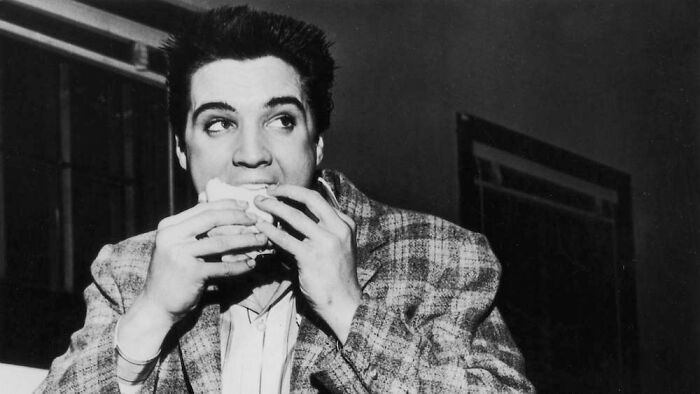 Black and white photo of a man eating a sandwich, capturing a bizarre throwback moment from past decades.