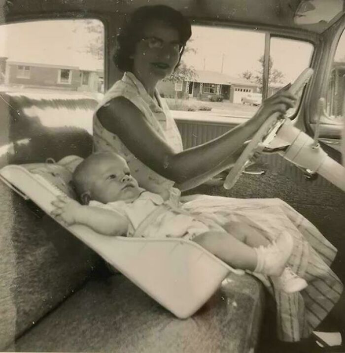 Vintage black and white photo of a woman driving with a baby lying unsecured in the front seat, a bizarre throwback moment.