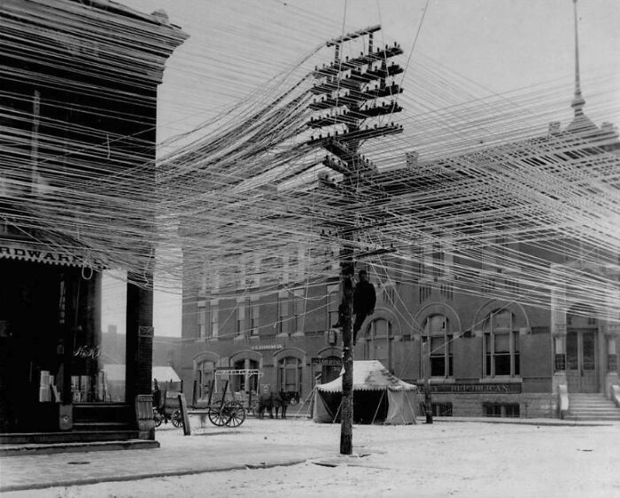 Vintage street scene showing a worker climbing a pole amid bizarre throwback moments with tangled overhead wires.