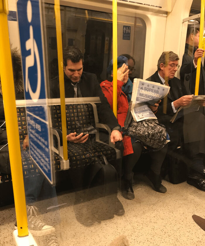 Passengers on a subway with a transparent man sitting next to a woman reading a newspaper causing confusion in unedited photo.
