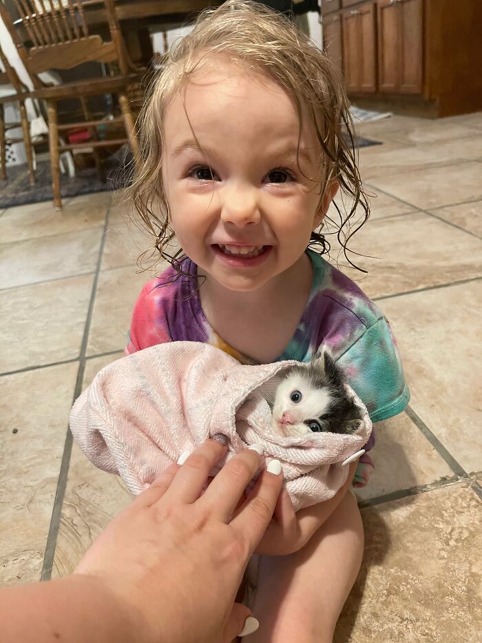 Young child smiling while holding a kitten wrapped in a towel, showcasing animals saved from awful conditions and given new life.