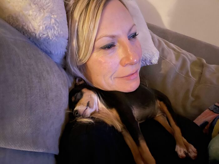 Woman resting on a couch with a small dog sleeping on her chest, showing animals saved from awful conditions.