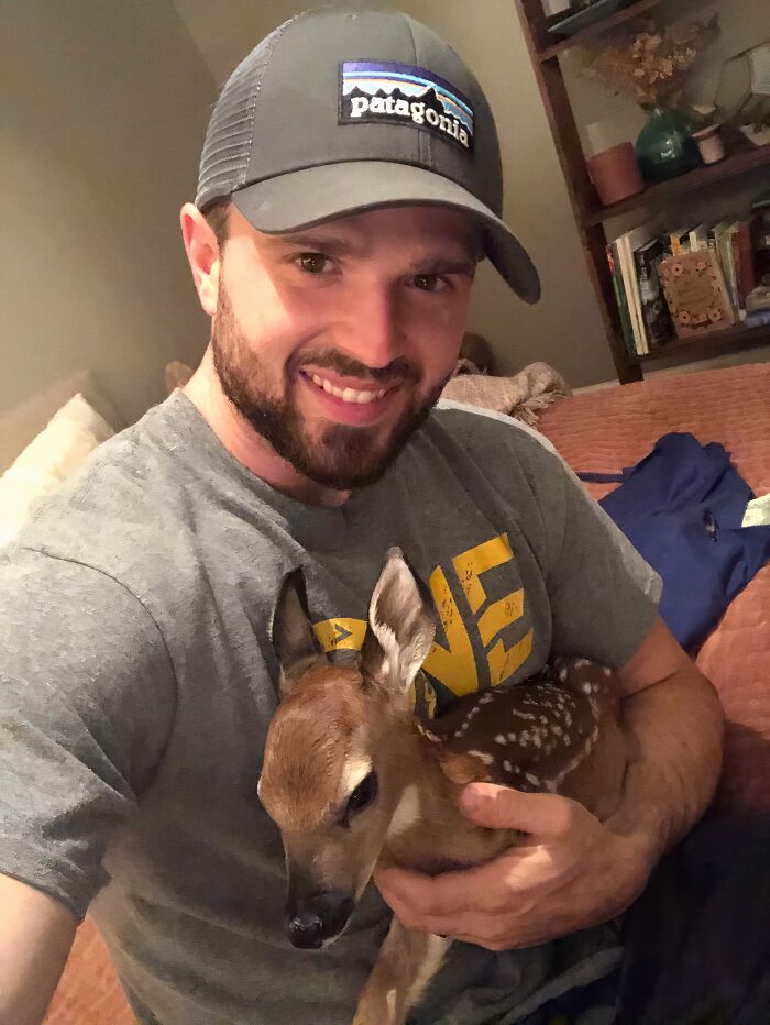 Man wearing a cap holding a rescued fawn, showcasing animals saved from awful conditions and given a second chance.