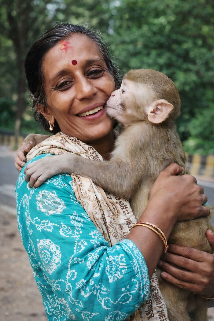 Woman smiling and holding a rescued monkey showing affection in a natural outdoor setting after a second chance in life.