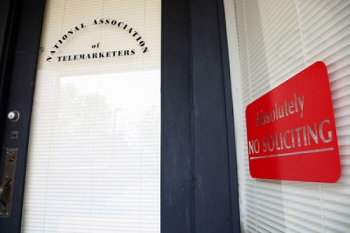 Entrance door of National Association of Telemarketers office with a red sarcastic no soliciting sign on the window.