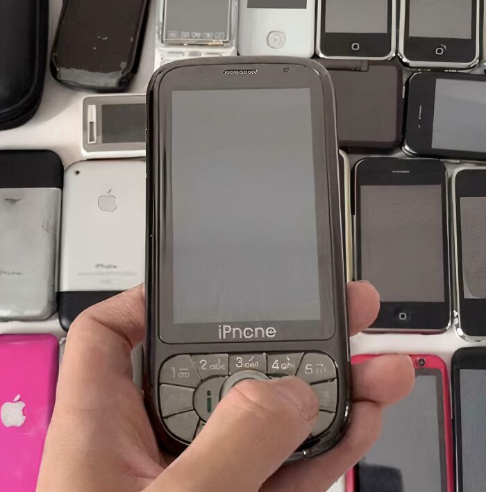 Hand holding a hilariously shamelessly copied iPhone lookalike phone among various old-style smartphones.