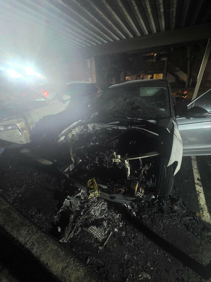 Severely burned and damaged car in a dark parking area illustrating neighbors that make you move to the middle of nowhere.