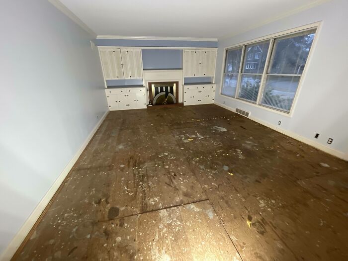 Empty living room with damaged unfinished floors and built-in cabinets, illustrating homes people regretted buying.